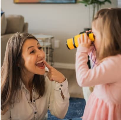Rosalyn laughing with a young child who is looking through toy binoculars
